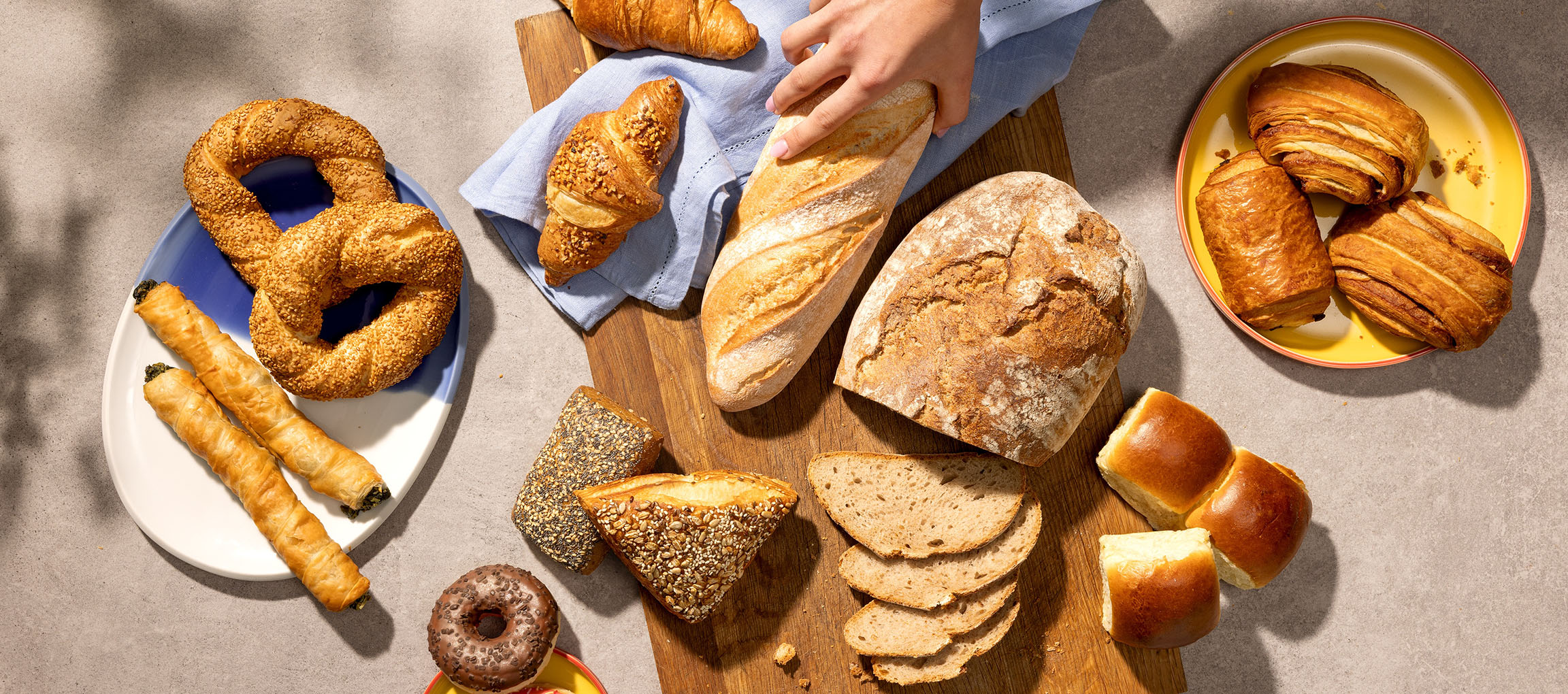 Assortment of pastries and bread, including pretzels, croissants, and baguettes, on a table.