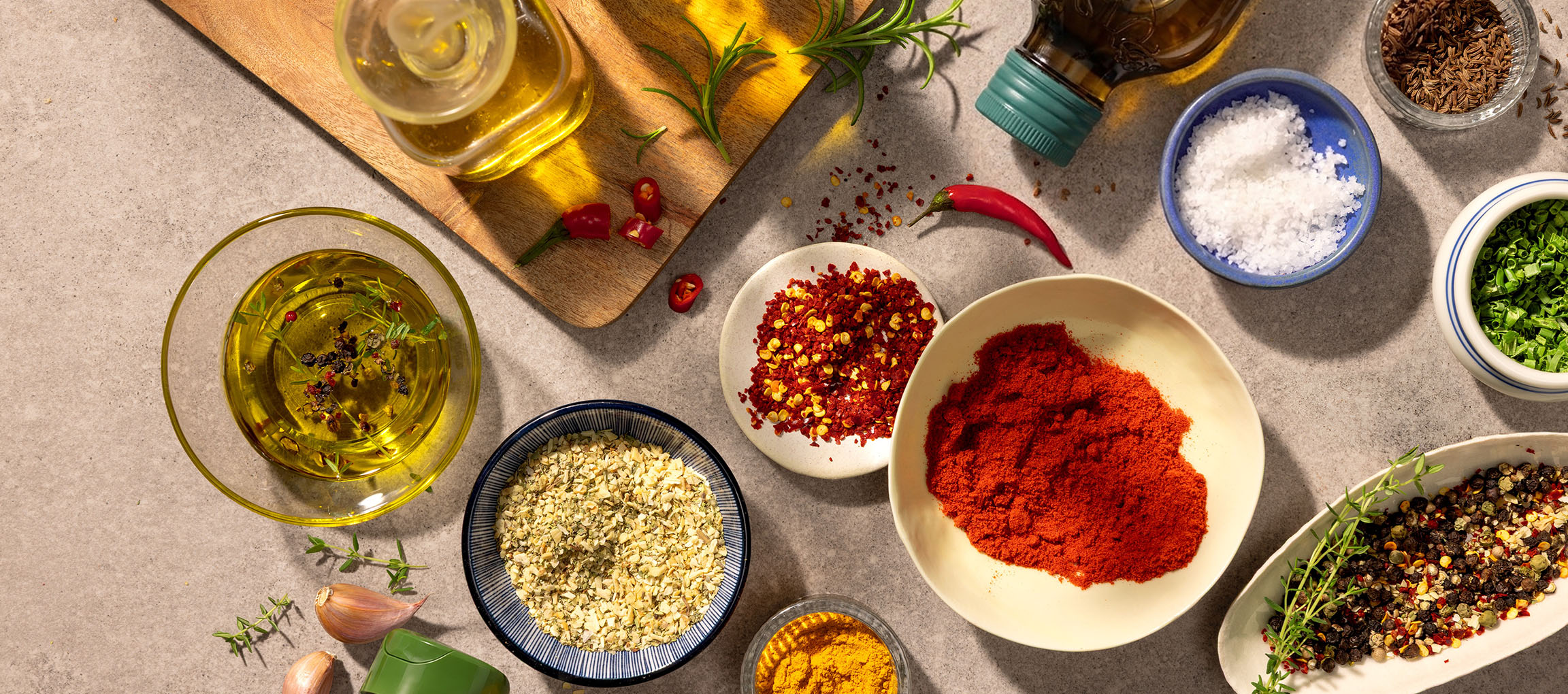 Olive oil, spices, and chili peppers on a wooden cutting board and stone table.