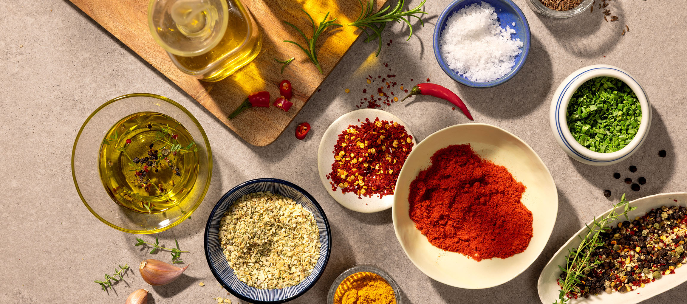Variety of spices and oils, including paprika, chili, salt, pepper, and olive oil, on a gray background.
