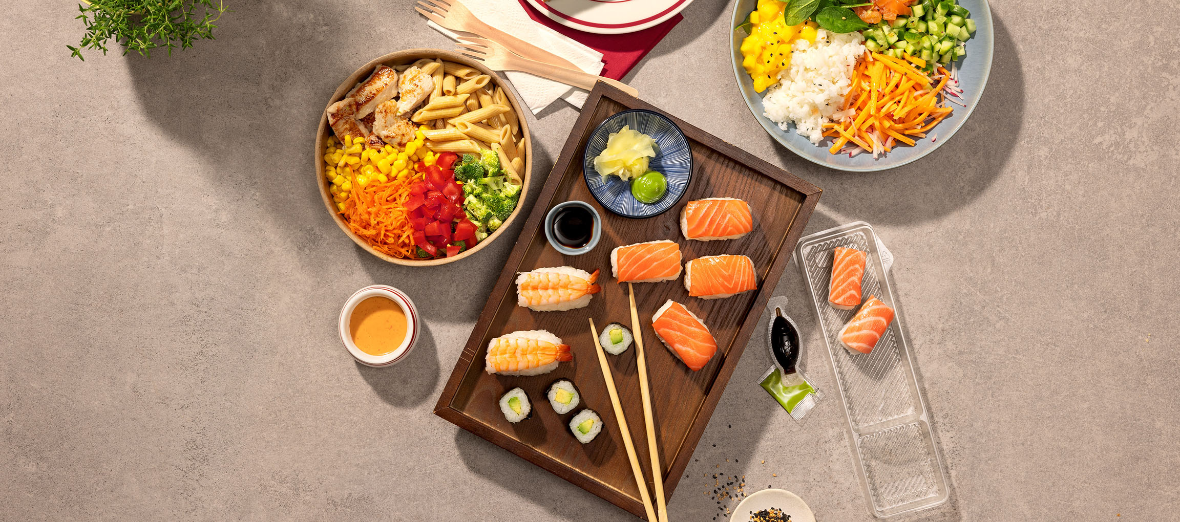 Assorted dishes: pasta and chicken bowl, sushi, and a poke bowl on a table.
