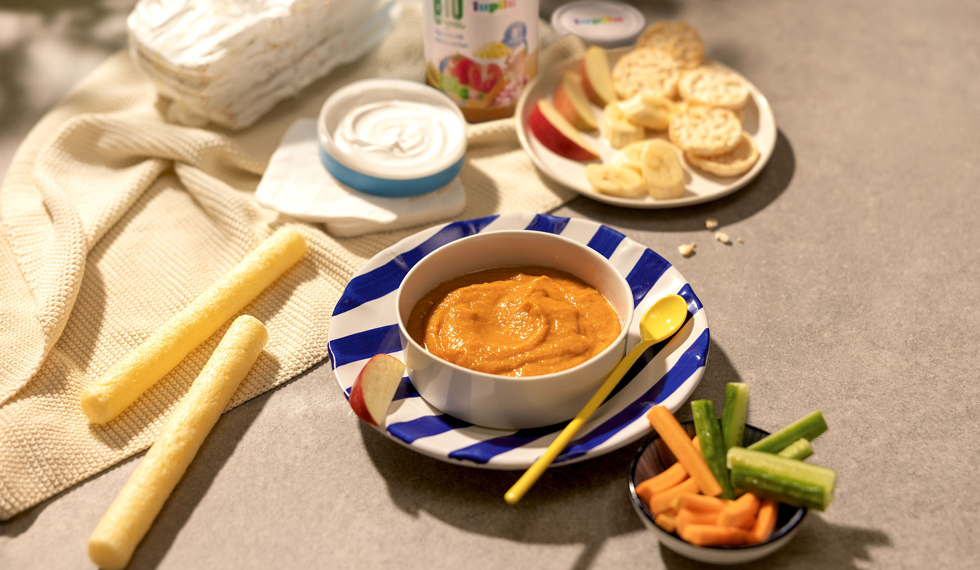 Baby food, yogurt, sliced fruit and vegetables, crackers, and snacks on a table.