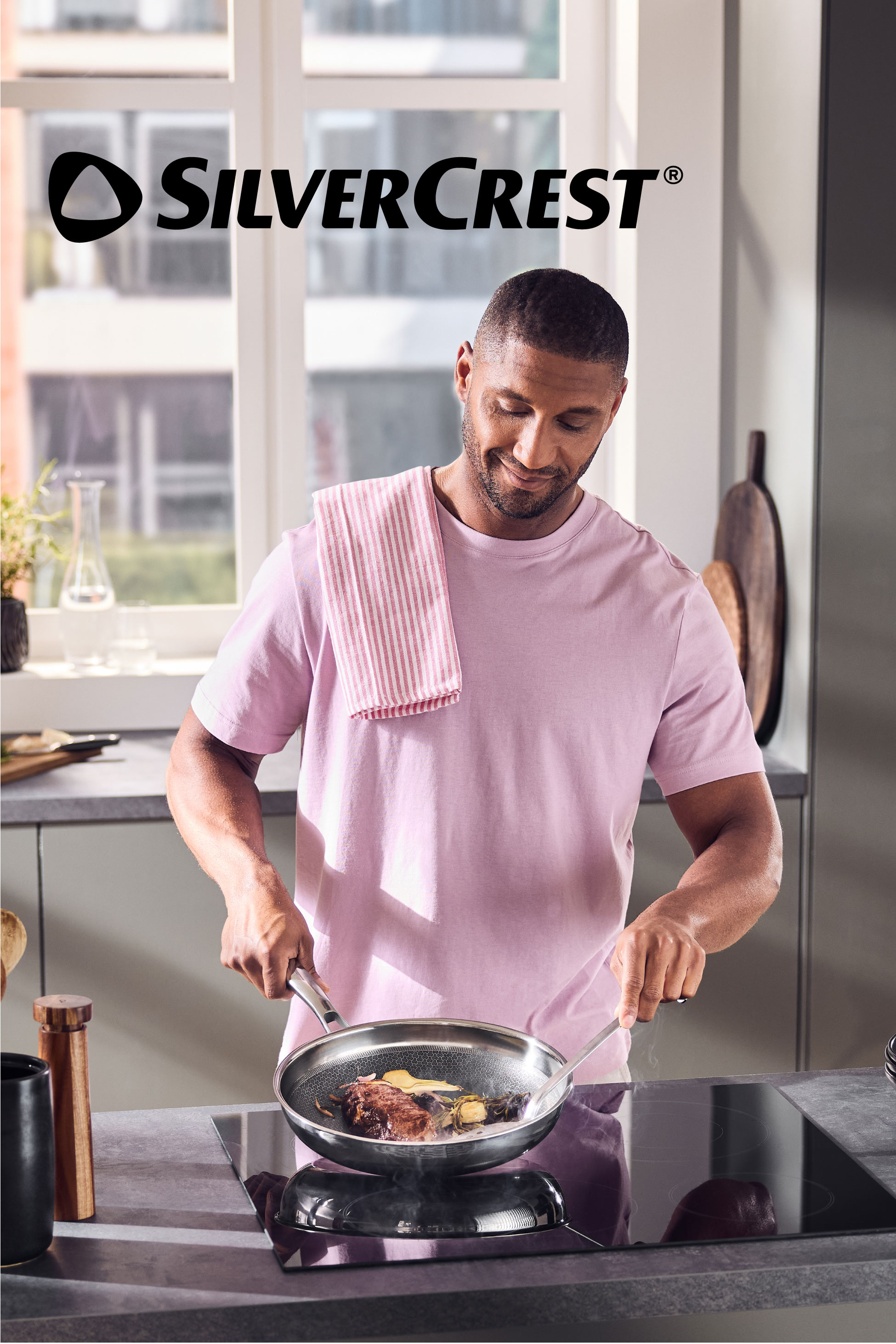 Man cooking steak and vegetables in a frying pan on an induction hob in a modern kitchen.