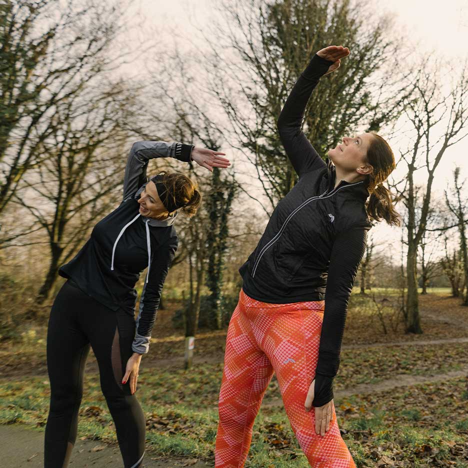 Two women in sportswear stretching outdoors.