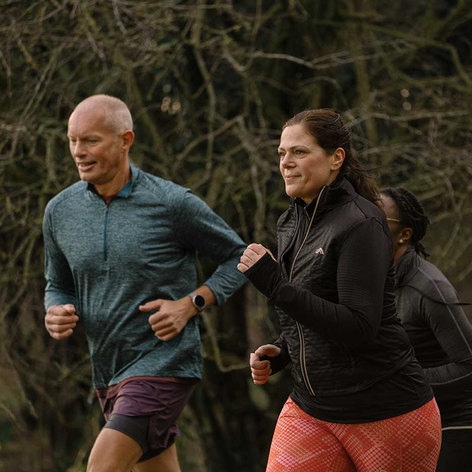 Two adult runners in athletic wear jogging outdoors.