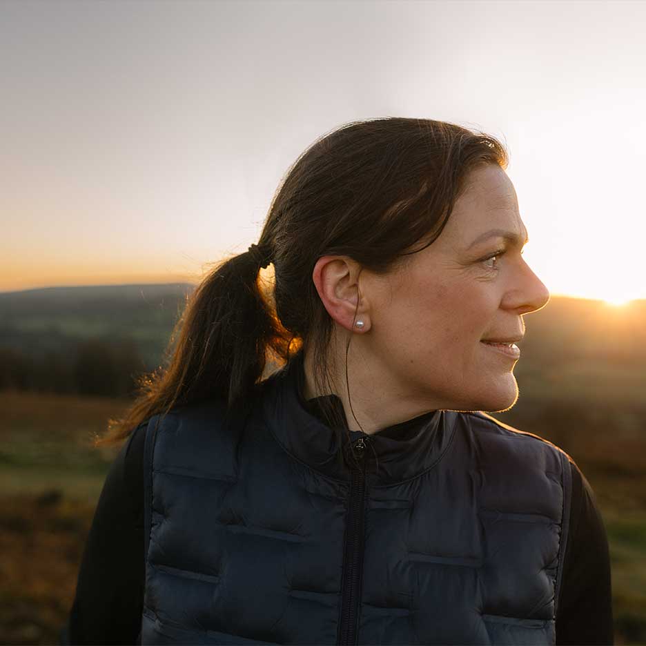 Woman in a black vest and black jumper at sunset.