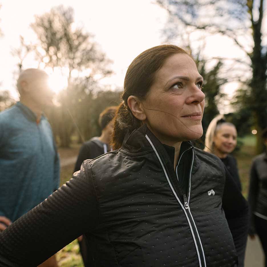 Woman in black sports jacket looking up, with a group of people in the background.