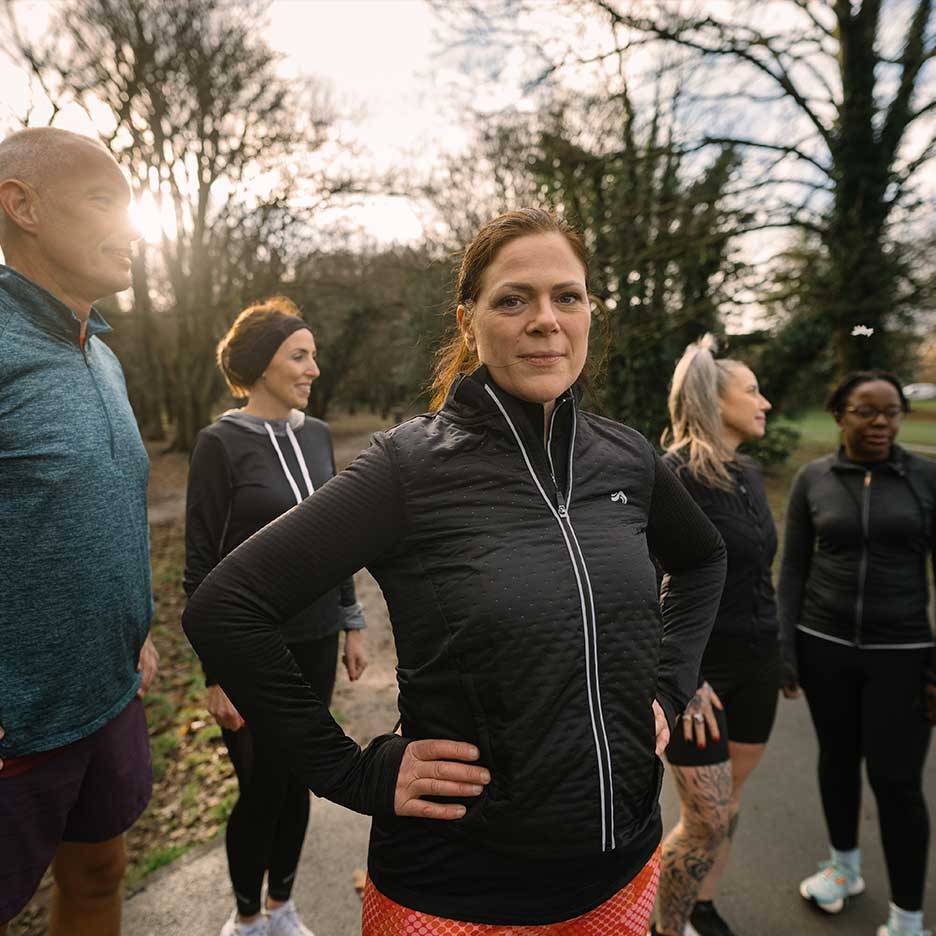 Group of people in activewear, including a woman in a black quilted jacket, outdoors.