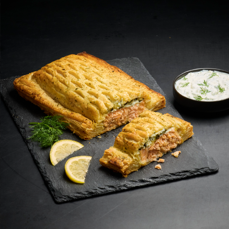 Salmon en croute with dill, lemon, and a side of tzatziki on a dark slate.
