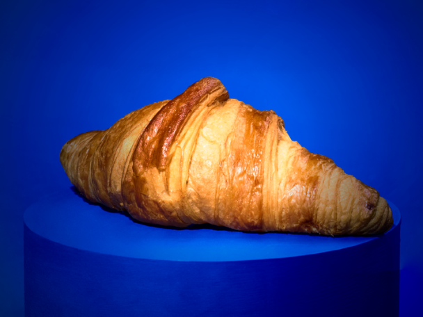 Golden-brown croissant on a vibrant blue circular platform.