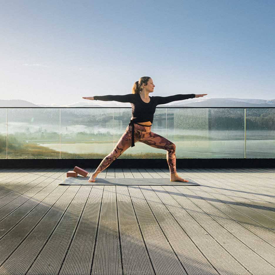 Woman in activewear leggings and top doing yoga on a terrace with a view.