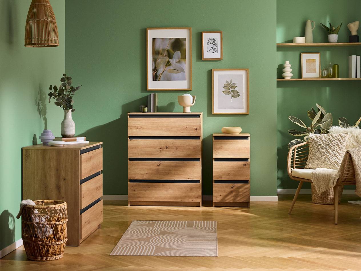 Living room with green walls, wooden dressers, shelves, and a rattan armchair.