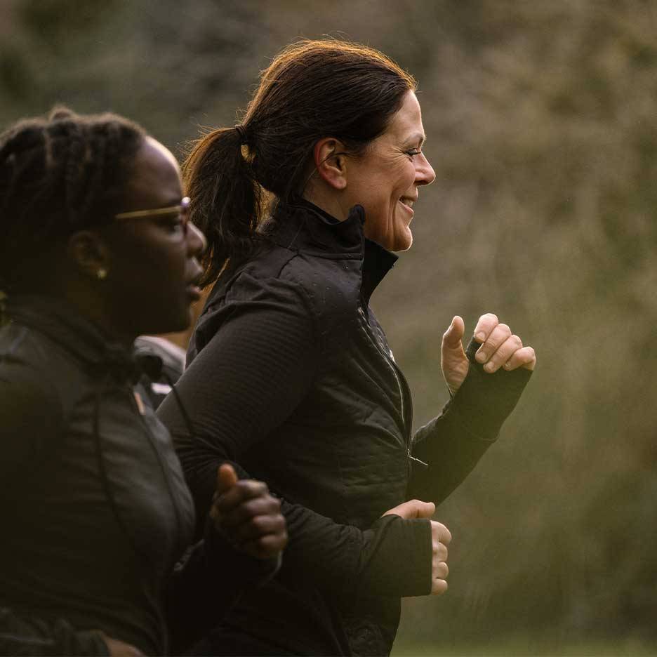 Two women in activewear running outdoors, one smiling.