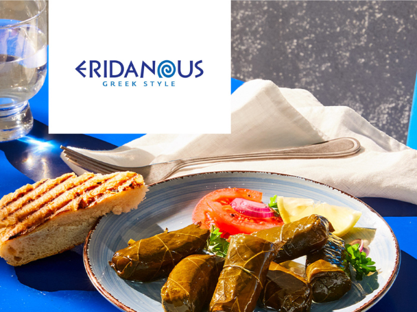 Greek-style stuffed vine leaves with grilled bread, tomatoes, and lemon on a blue table.