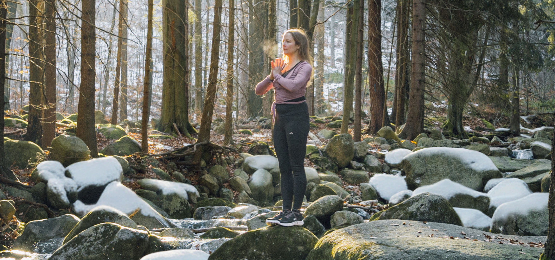 Woman in activewear doing yoga in a snowy forest with a stream.