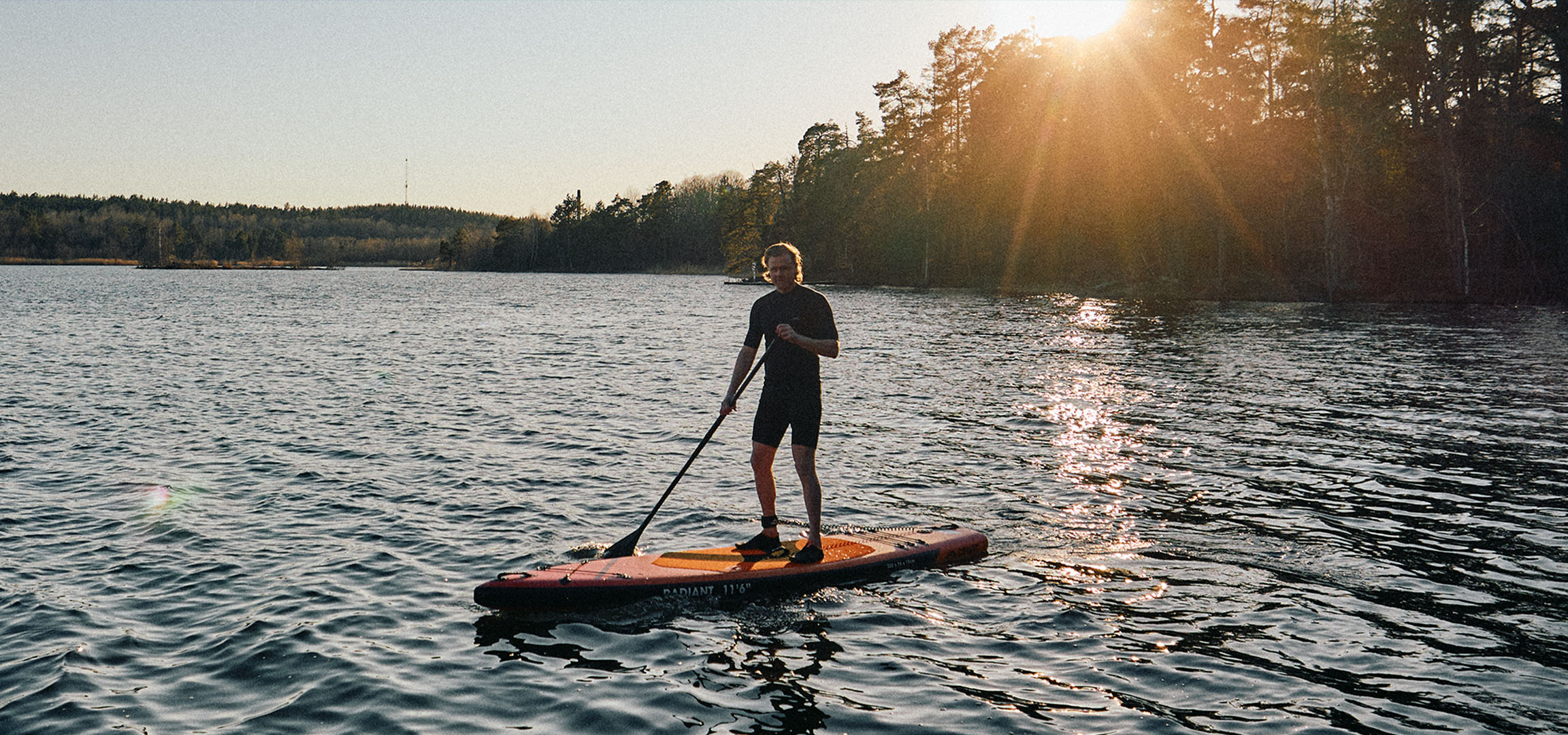 Man on a stand-up paddleboard on a lake at sunset.