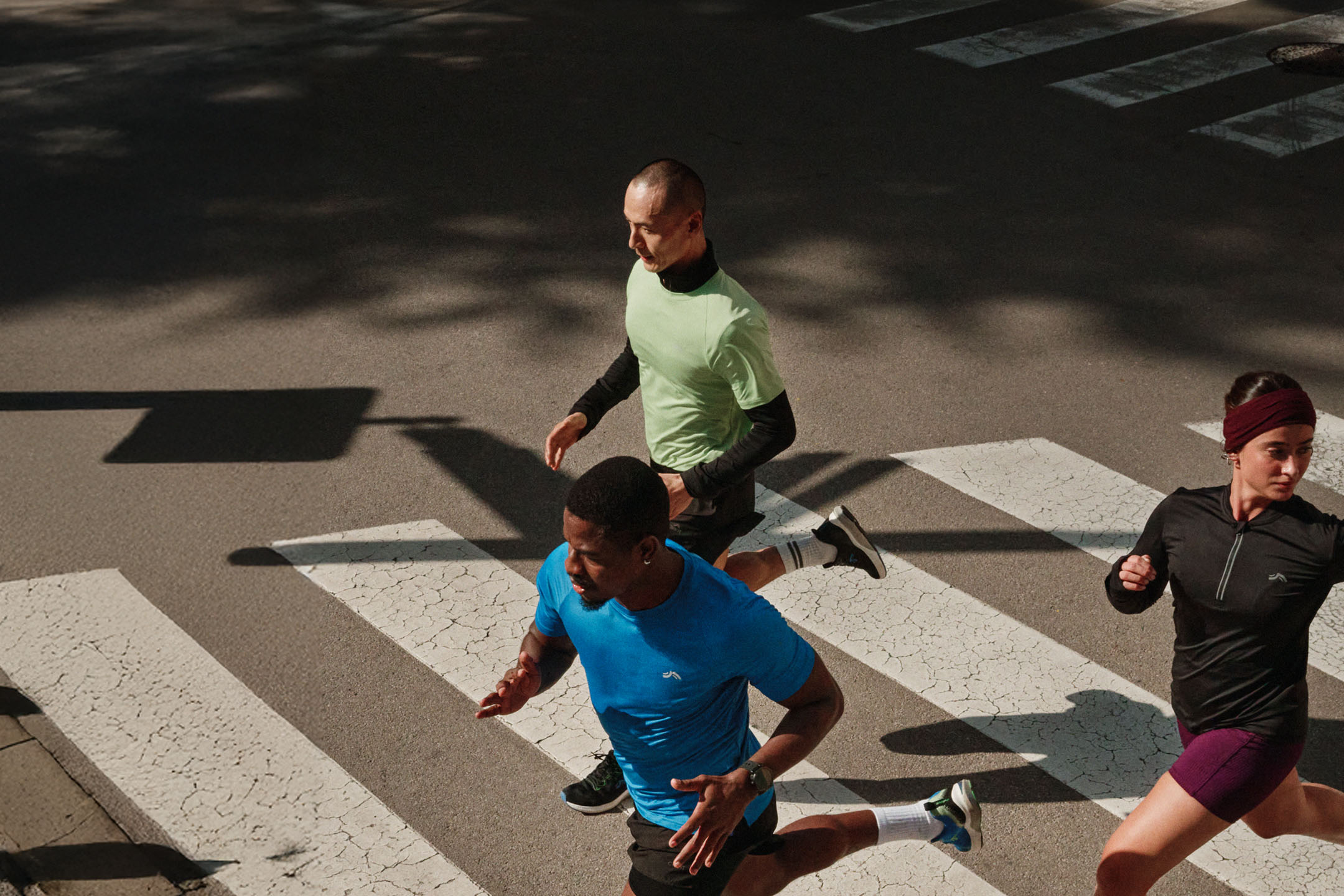 Three runners in colorful sportswear crossing a pedestrian crossing.