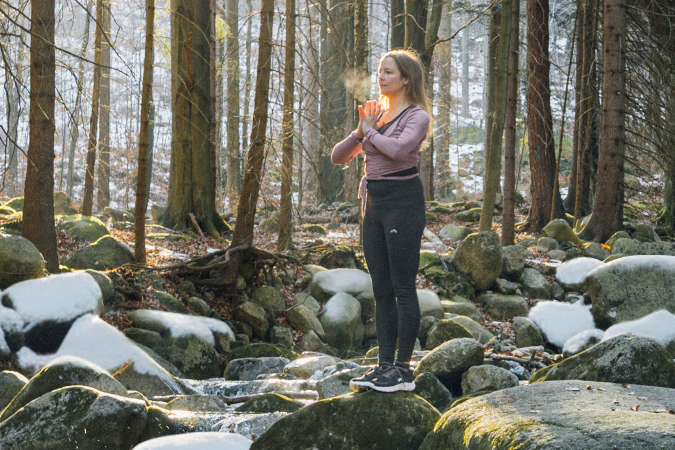 Woman in sportswear practicing yoga in a winter forest by a stream.
