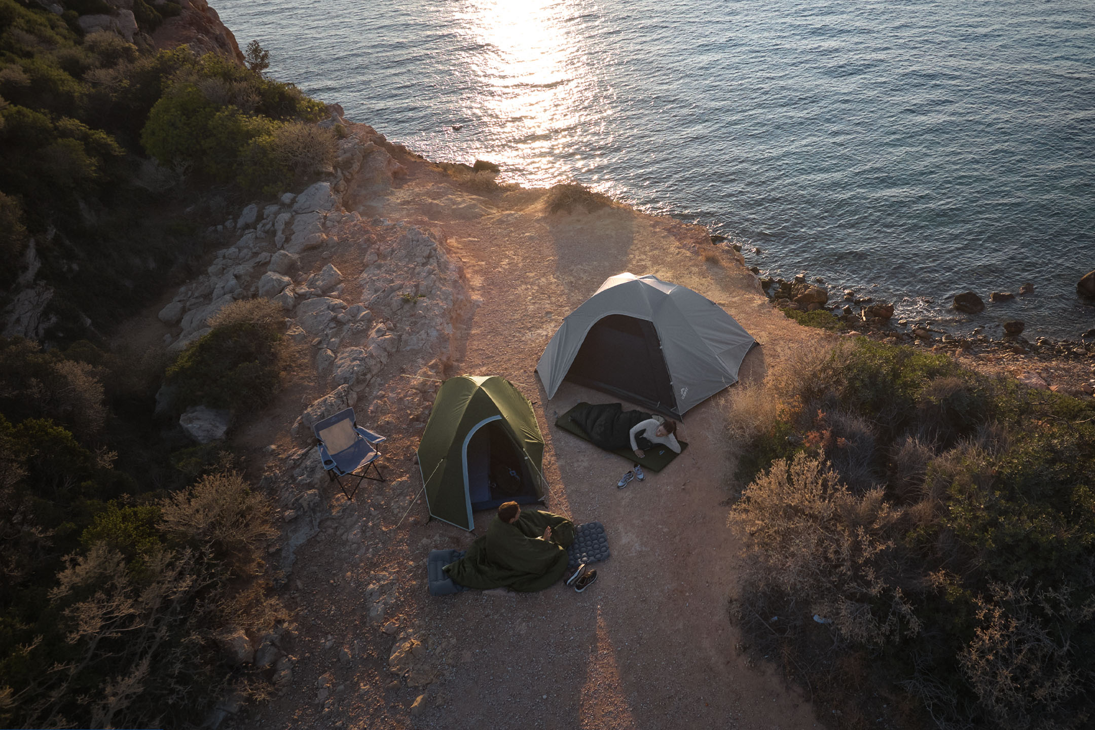 Two tents and campers on the coast, one in a sleeping bag, the other on a sleeping mat.
