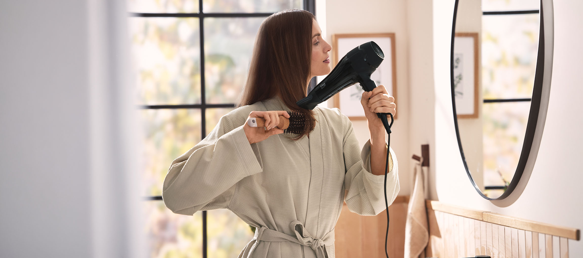 Woman drying her hair with a hairdryer and brush in the bathroom.