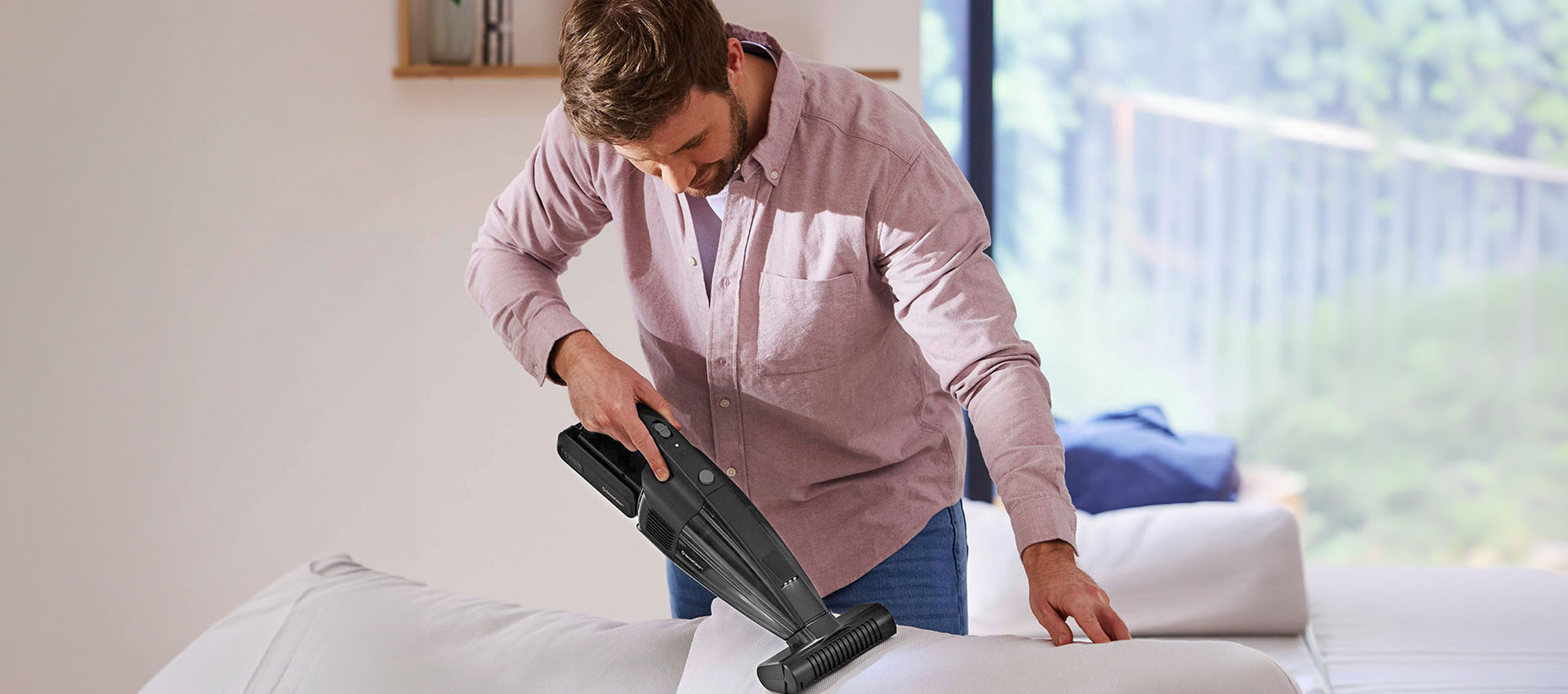 Man cleaning a sofa with a handheld vacuum cleaner.