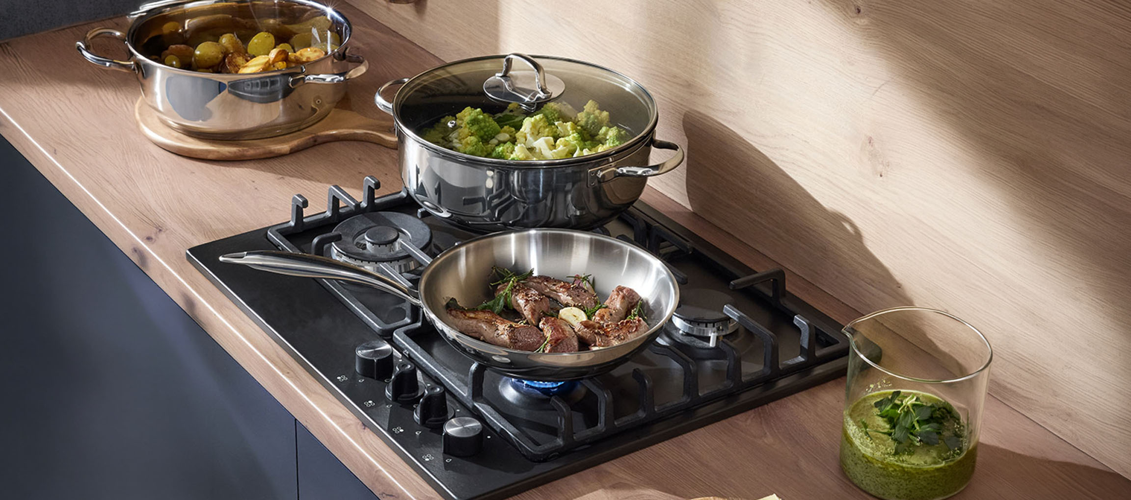 Gas hob with stainless steel pots and pans filled with vegetables and meat.
