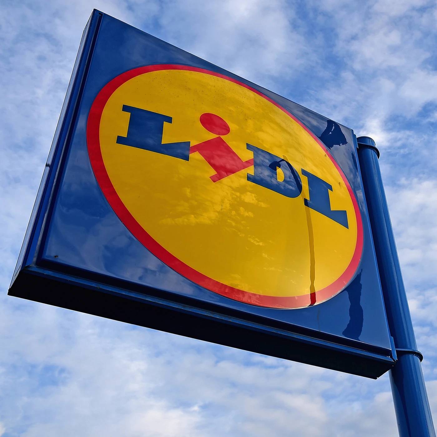 A blue and yellow Lidl sign with red accents against a cloudy sky.